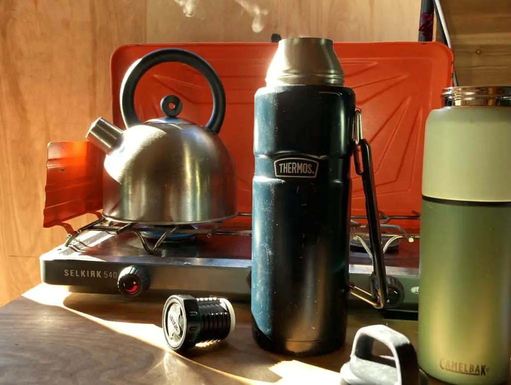 Black Thermos Next To Silver Kettle On Stove