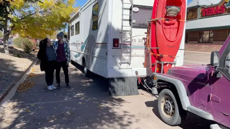 White RV Parked In Front Of Purple Jeep With Driver Owners Standing Next To It 